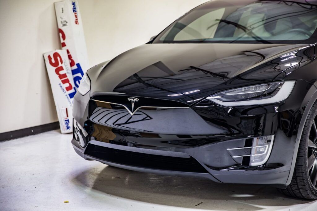 Black Tesla SUV parked indoors, with window tinting materials visible in the background.