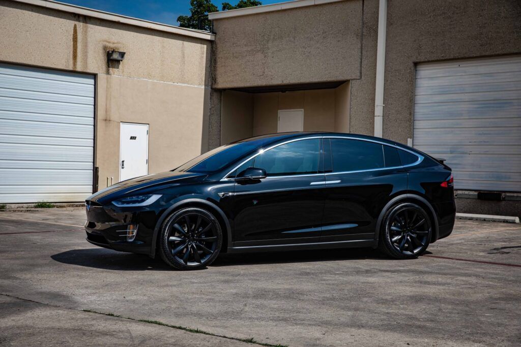 Black Tesla Model X parked outside a tan industrial building.