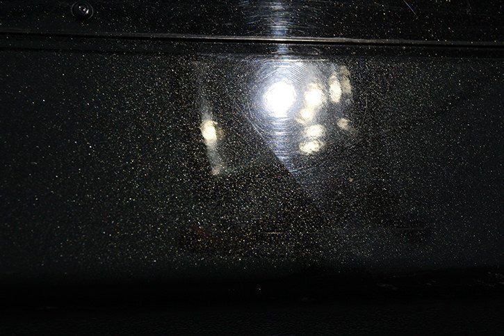 Dust and smudges on a dark, shiny surface, with a bright light source reflected.
