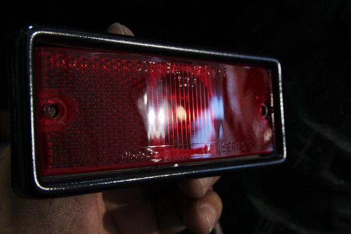Red rectangular tail light with black frame, held by a hand.
