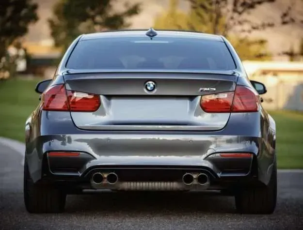 Rear view of a dark gray BMW M3 sedan with dual exhaust pipes, red taillights, and the BMW logo.