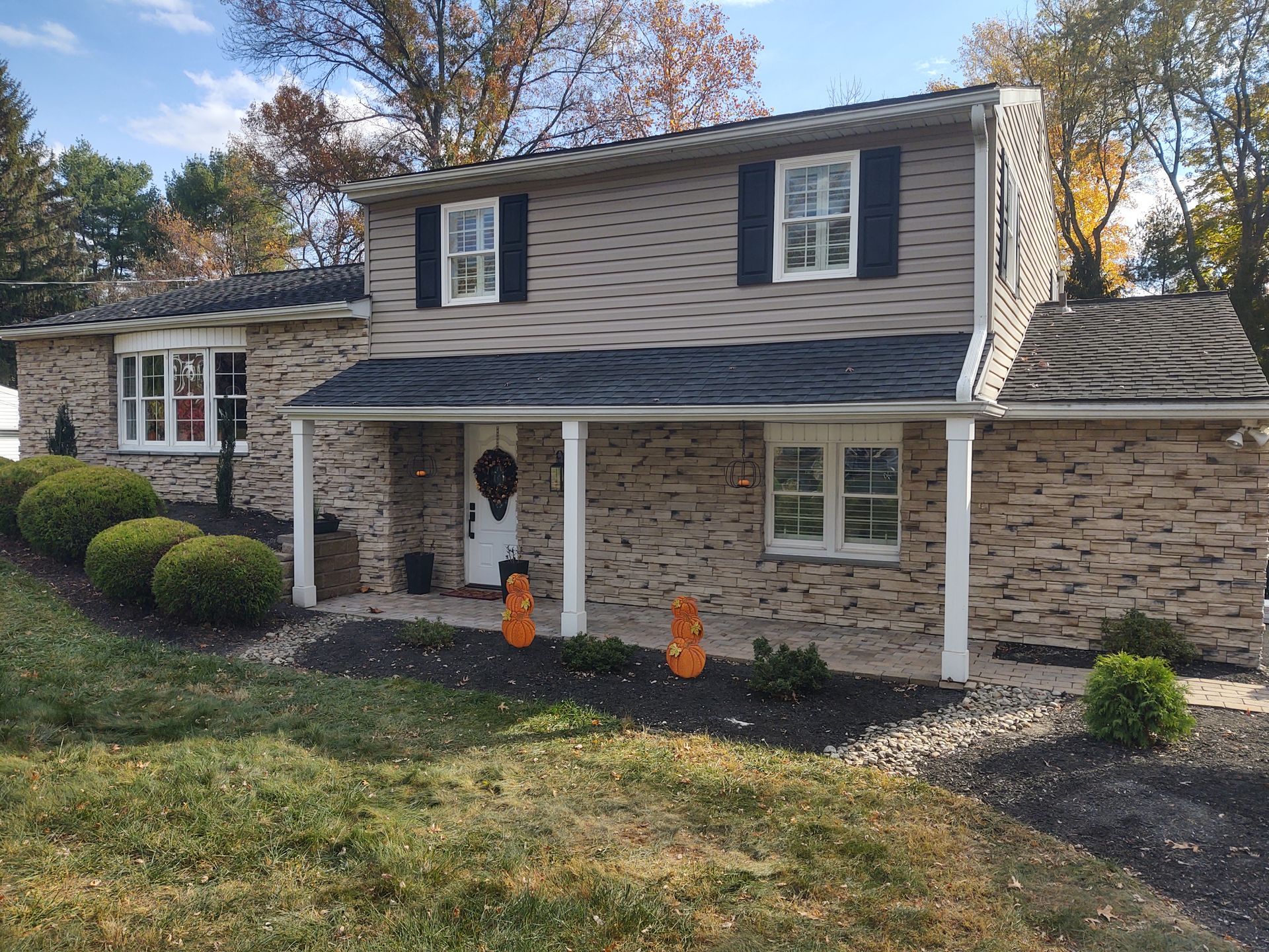 A Large Brick House with A Porch and Pumpkins in Front of It.