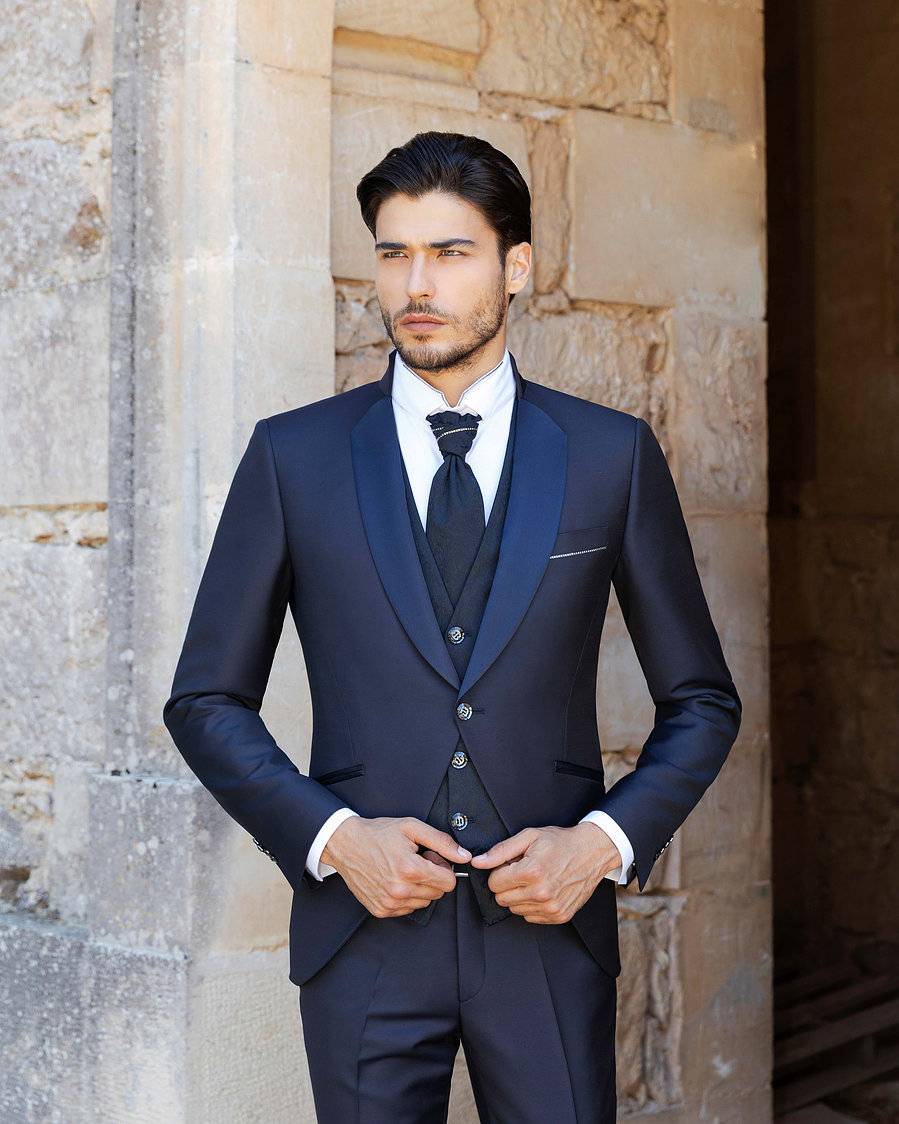 Homme portant un costume de mariage bleu marine devant une façade en pierre