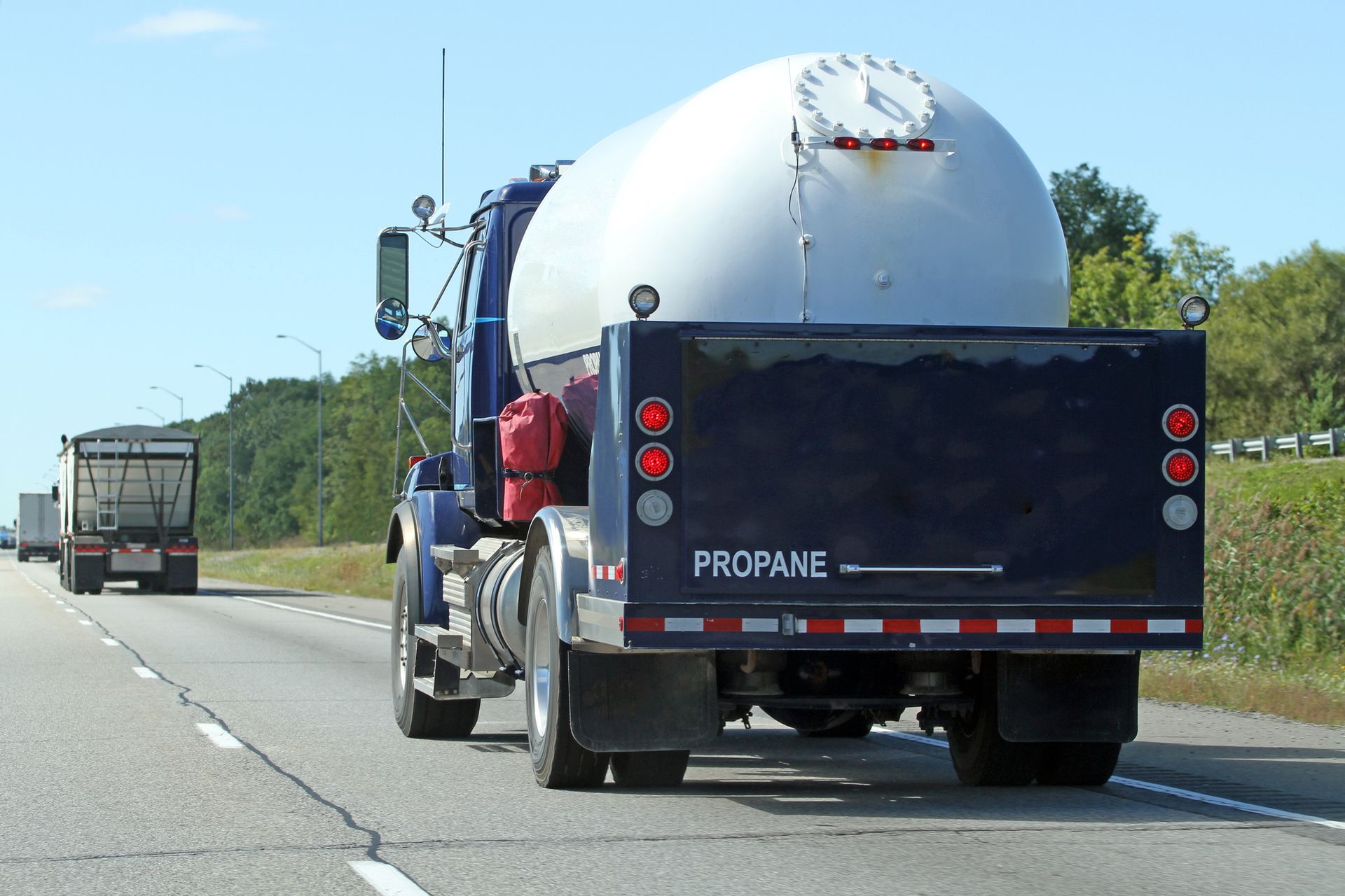 Propane delivery truck driving on interstate highway from a rear side angle during transport.