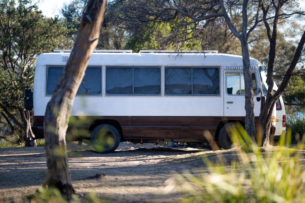 A White Bus is Parked in a Dirt Lot Surrounded by Trees โ Ozzie Camper Trailers in Aitkenvale, QLD