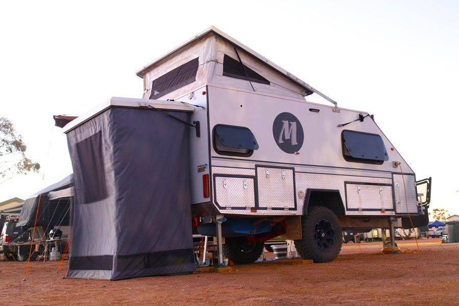 A White Trailer With the Letter M on the Side is Parked in a Dirt Field — Ozzie Camper Trailers in Aitkenvale, QLD