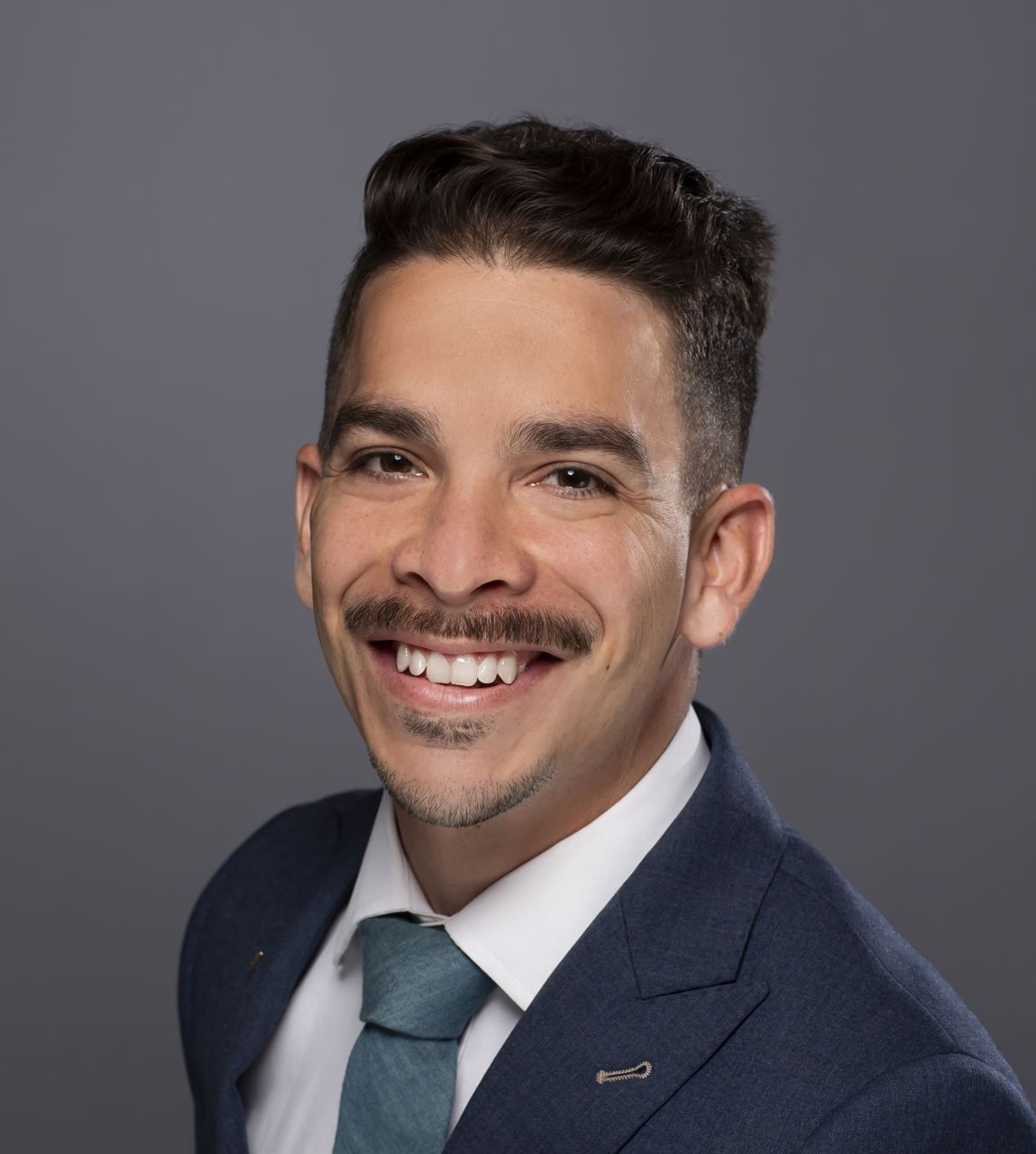 Smiling man in a navy suit and tie against a gray background