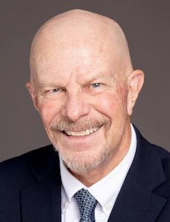 Smiling bald man in a dark suit and tie on a gray background
