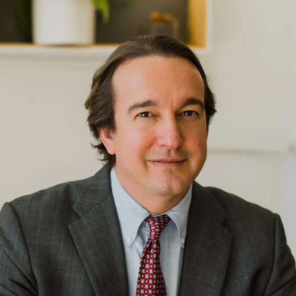 Portrait of a man in a gray suit and red tie, smiling in an office setting