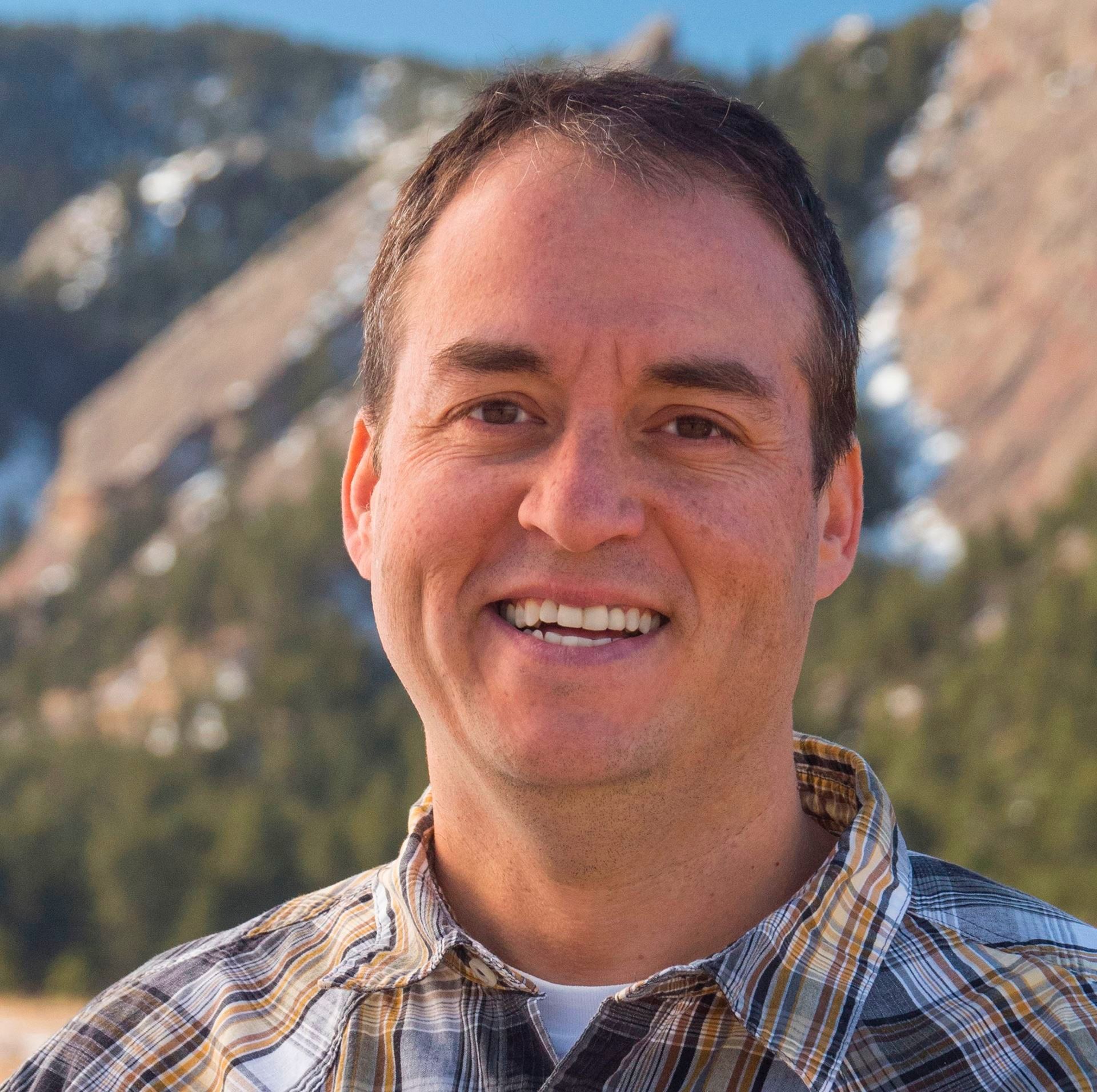 Smiling man in plaid shirt outdoors with mountains in the background