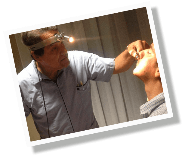 Un hombre está examinando la boca de otro hombre con una luz en su cabeza.