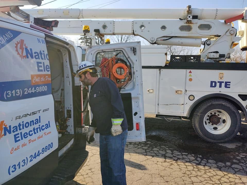 Utility worker beside National Electrical truck and white DTE bucket truck on a sunny street