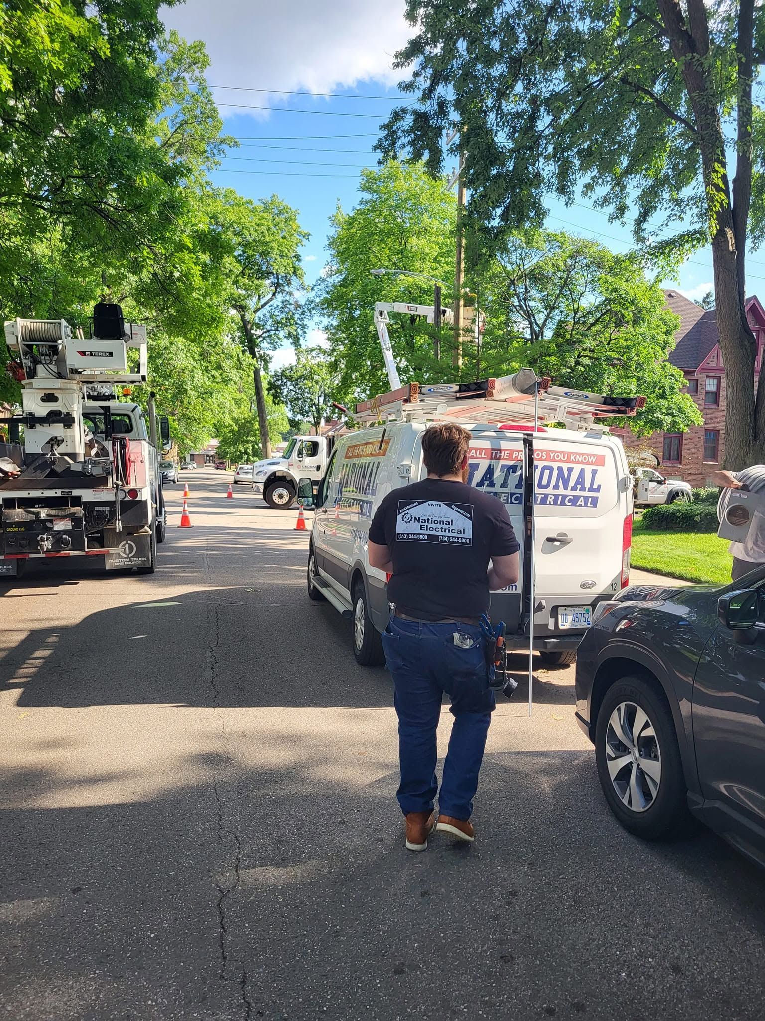 Street with utility trucks and workers under leafy trees on a sunny day