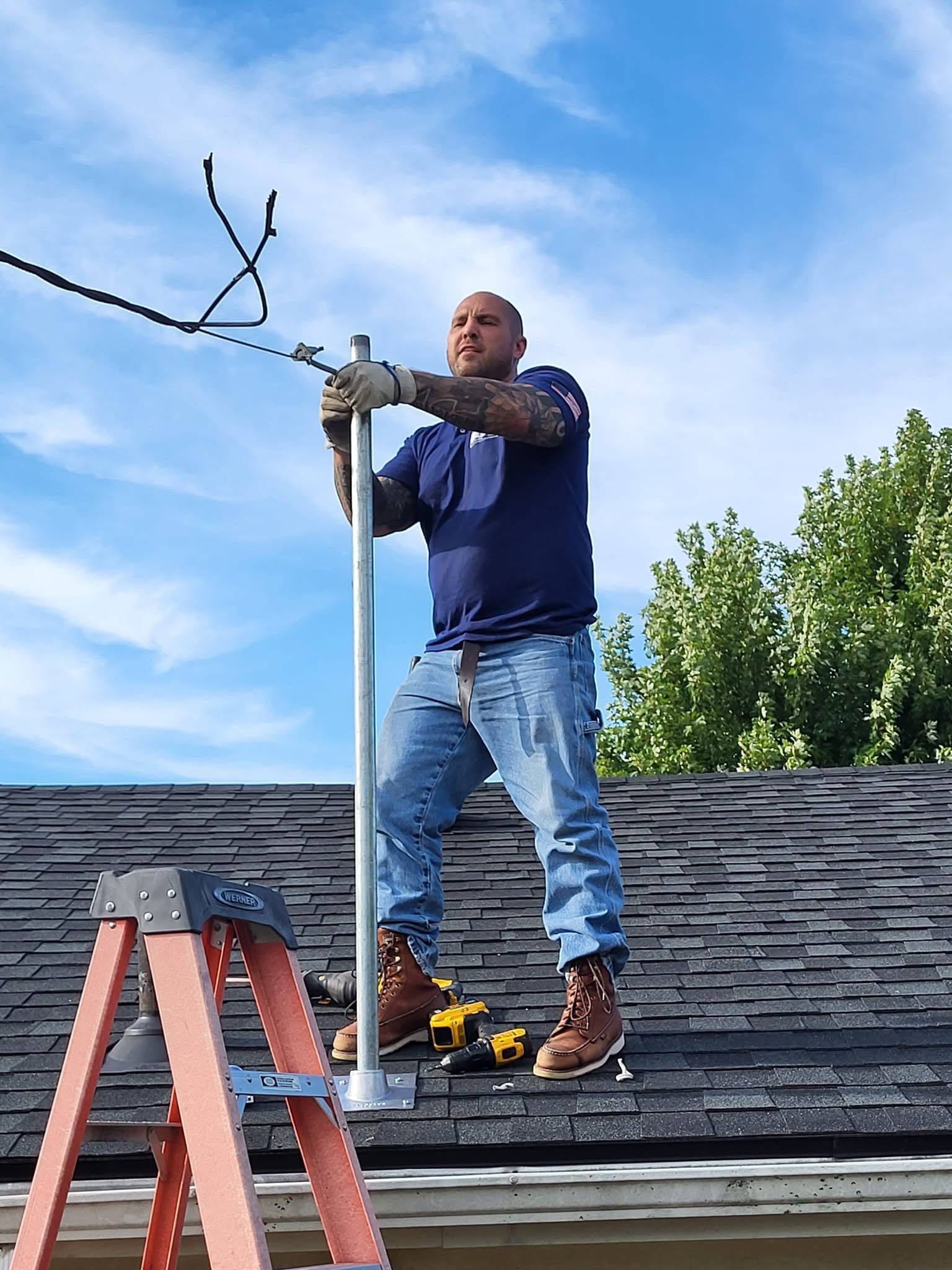 Worker on a roof adjusting a TV antenna beside a red ladder on a sunny day