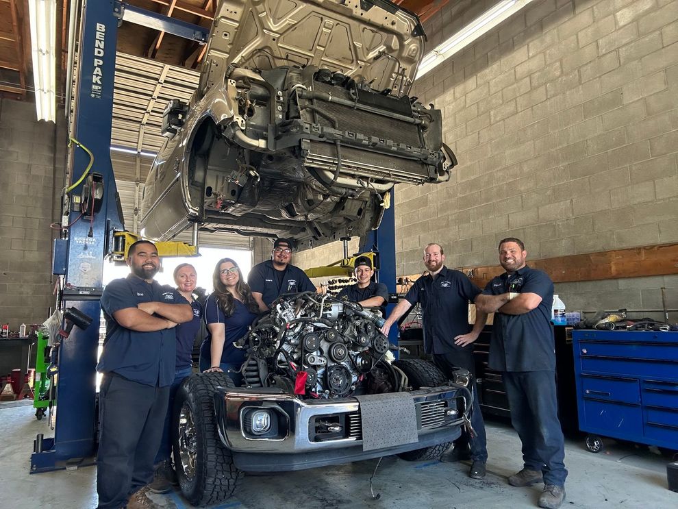 A group of mechanics are standing in front of a car with the hood up.