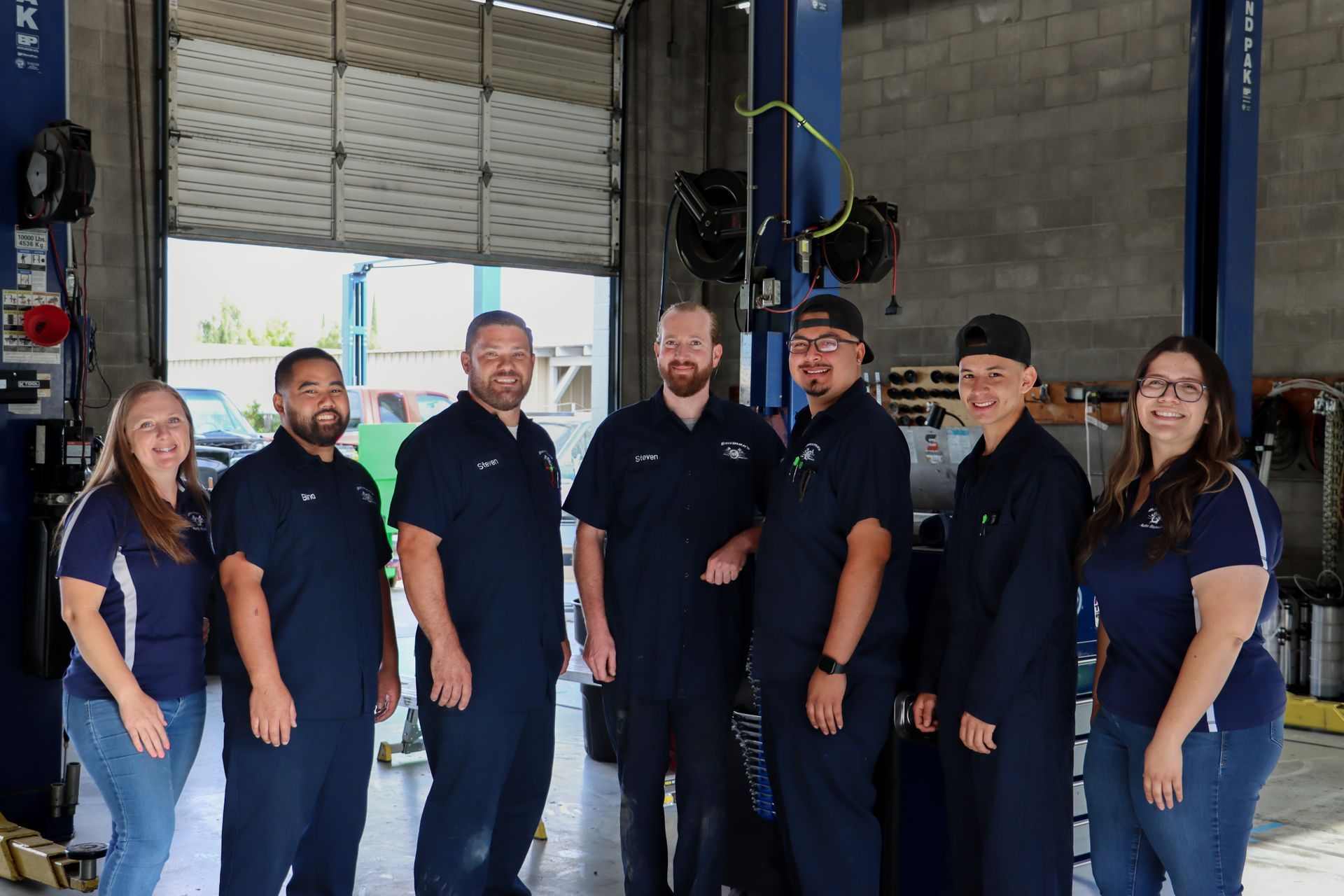 A group of mechanics are posing for a picture in a garage.