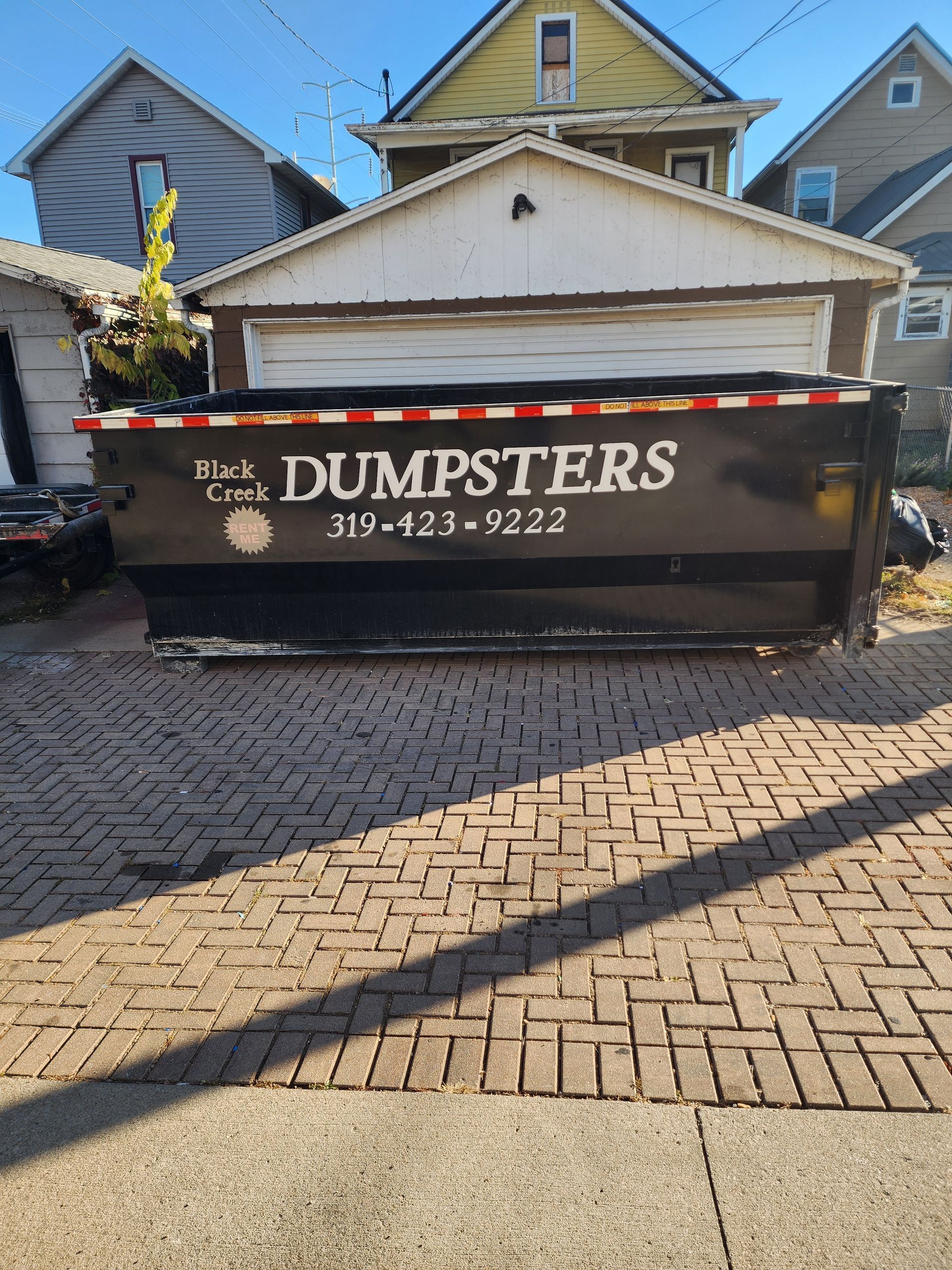 Black dumpster on trailer parked on driveway.