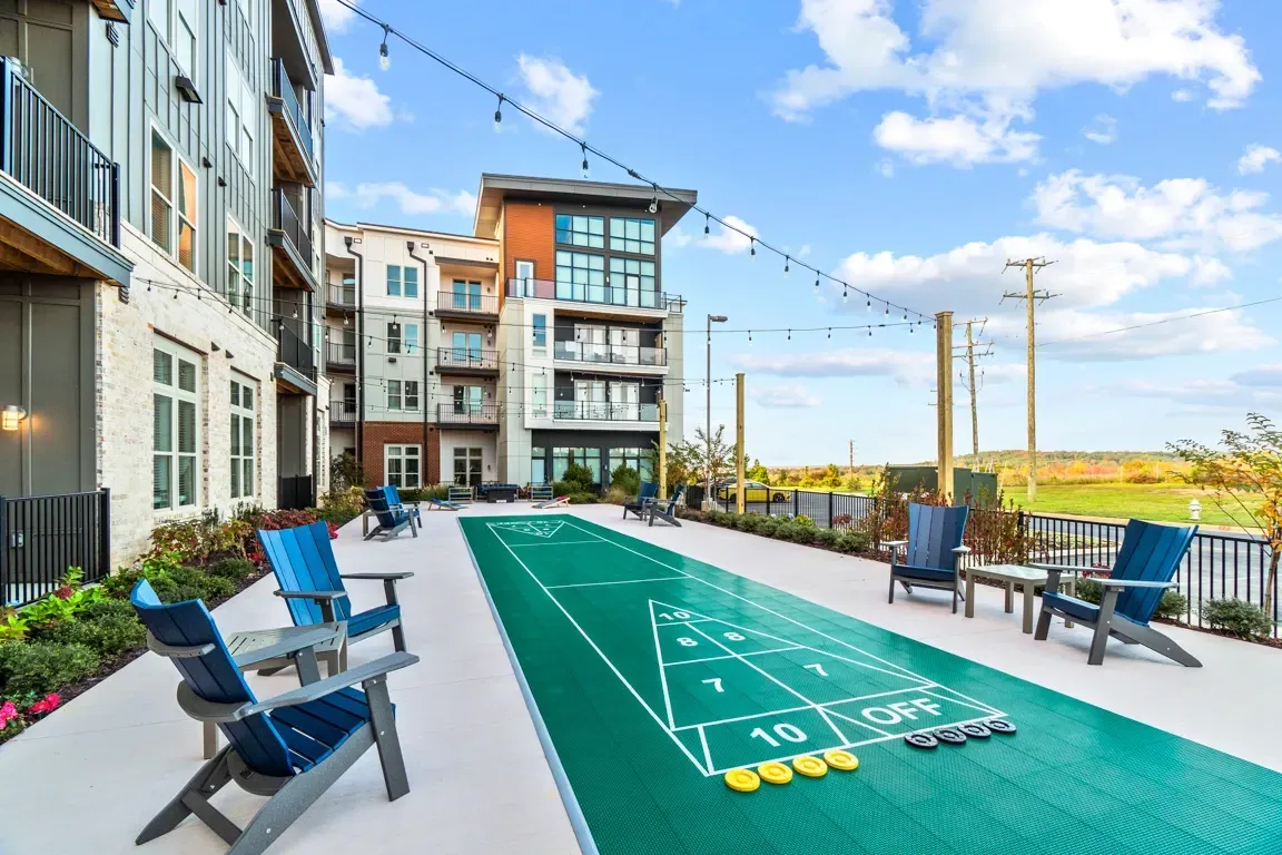 Shuffleboard court with seating area and apartment buildings in the background.