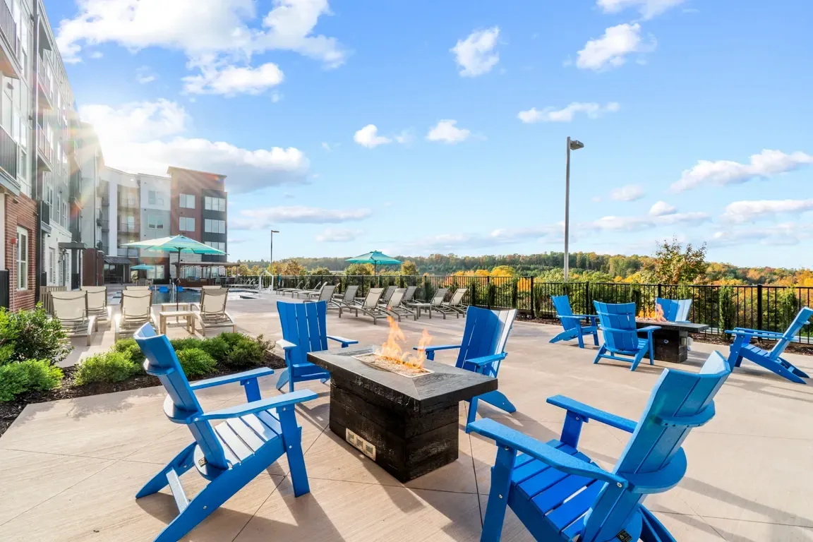 Outdoor patio with blue Adirondack chairs around a fire pit, lounge chairs, and a pool in the background.