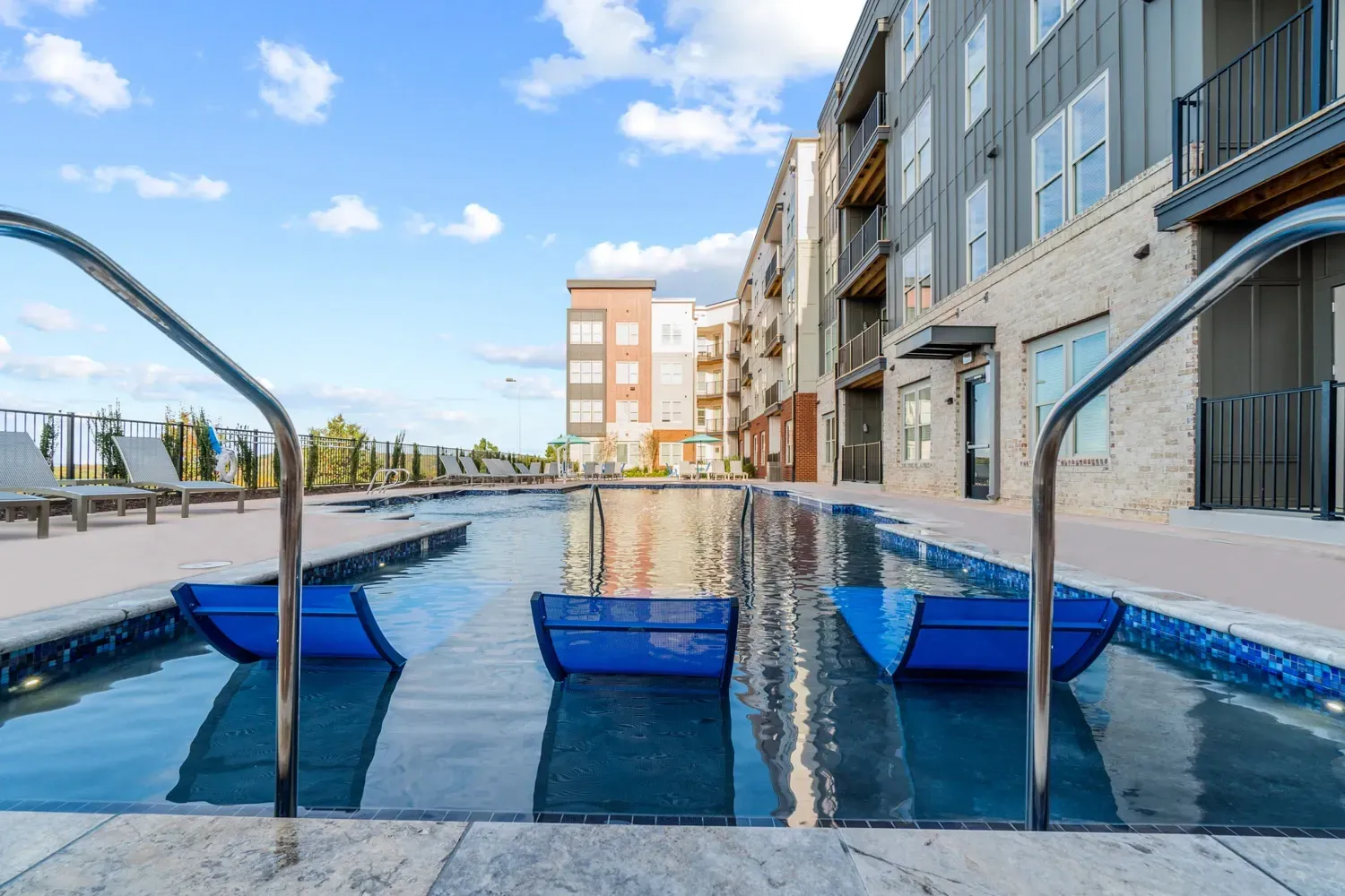 Modern swimming pool with submerged loungers and lounge chairs nearby.