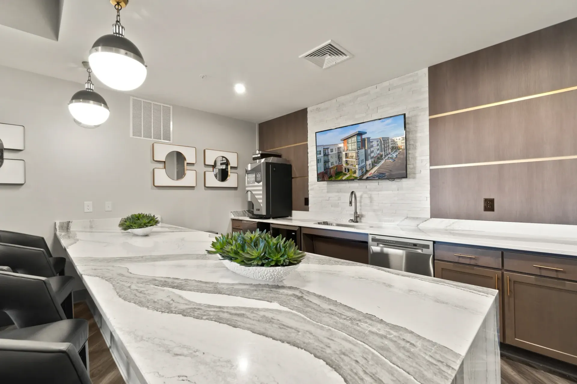 Kitchenette area with a large marble countertop, coffee machine, sink, dishwasher, and a TV displaying an exterior building view.