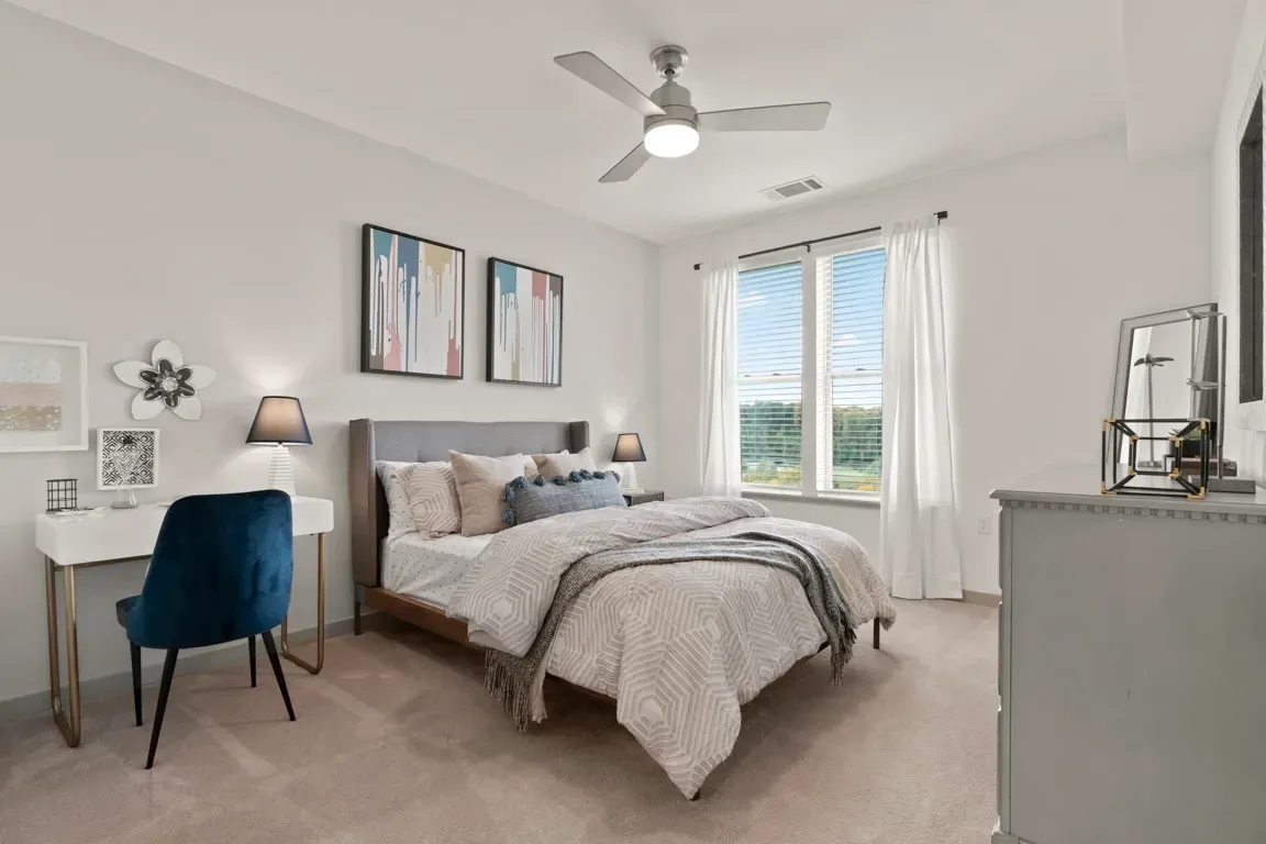 Cozy bedroom with a queen-size bed, white desk, and blue chair.