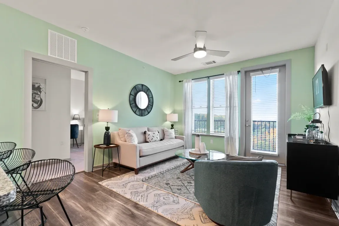 Modern living room with light green walls, a couch, coffee table, and accent chair, with a view from the balcony.