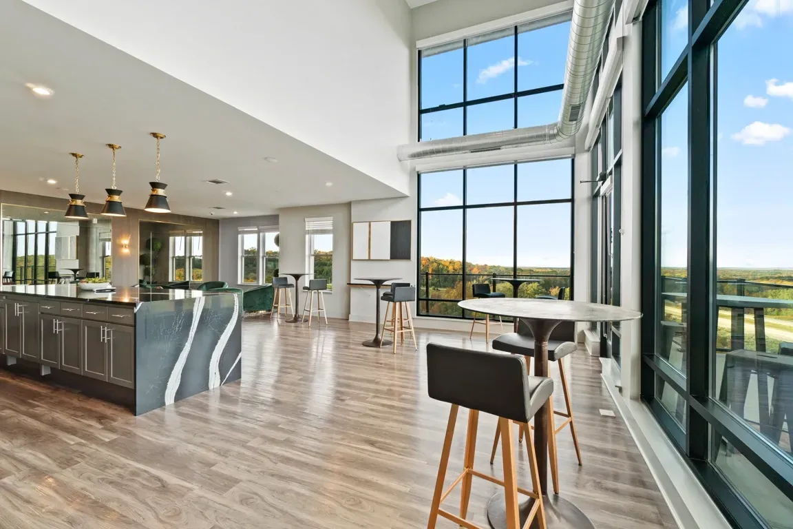 Modern lounge area with a large island kitchen, high ceilings, and expansive windows with a scenic view.