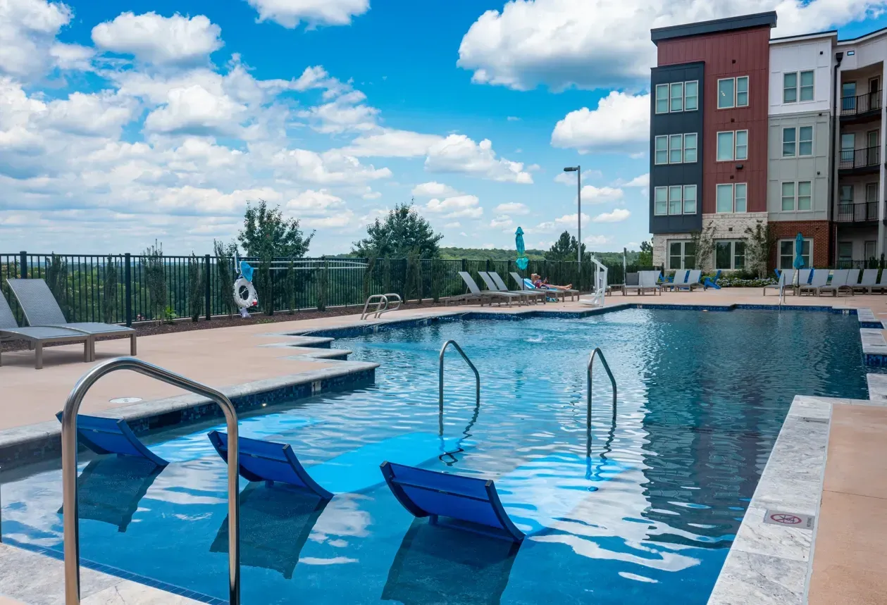 Outdoor swimming pool with lounge chairs and a modern apartment building in the background.