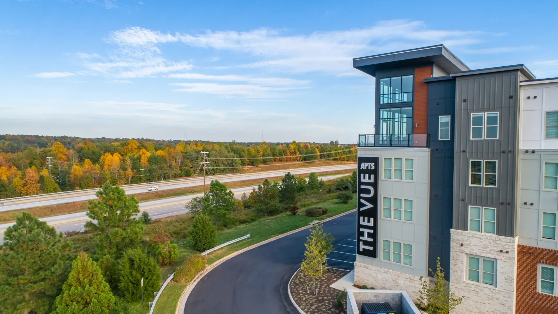The Vue apartments building exterior with surrounding trees and a highway.