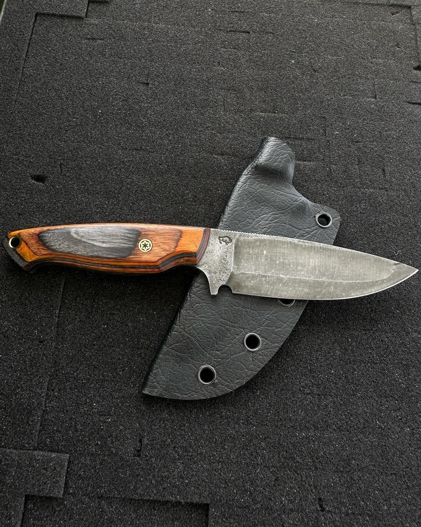 Fixed blade knife with wooden handle and textured metal blade in a black sheath.