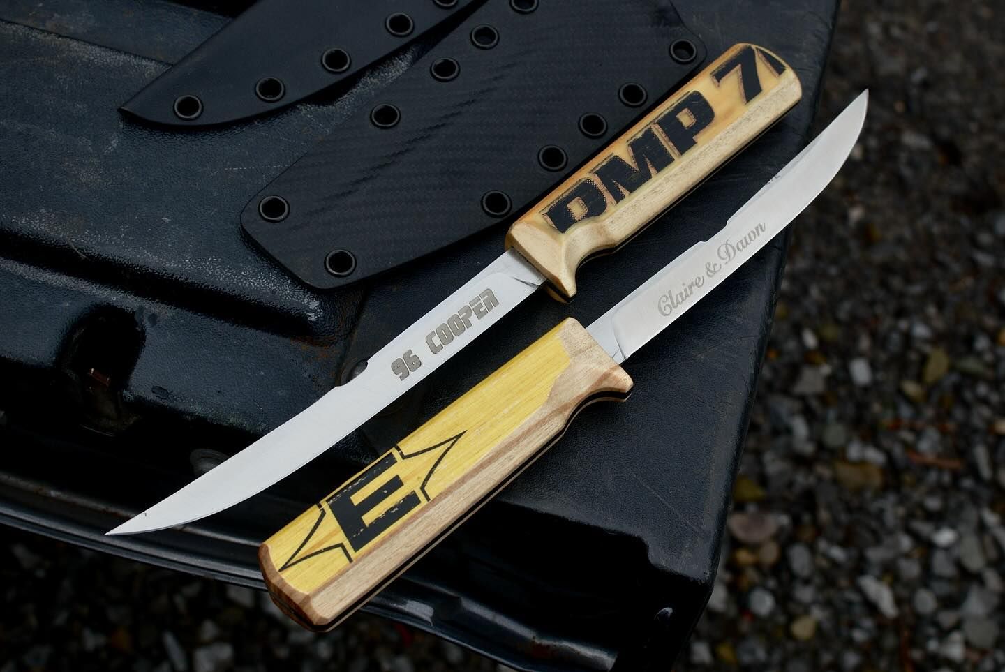 Two knives with wooden handles and black sheaths on a dark textured surface.