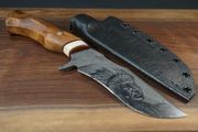 Knife with wooden handle, Native American etching on blade, leather sheath on a wood surface.