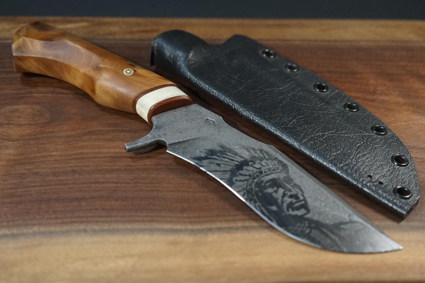 Knife with wooden handle and Native American portrait etched on the blade, next to a black leather sheath