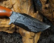 Damascus steel knife with brown handle, resting on a textured wooden surface.