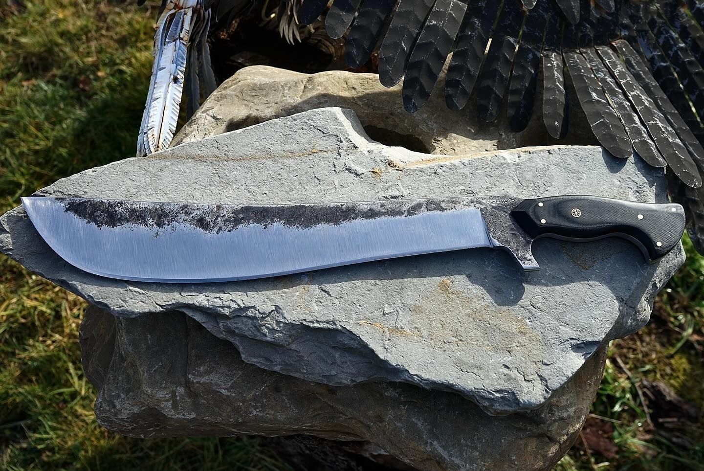 Large, curved blade knife resting on a gray rock outdoors.