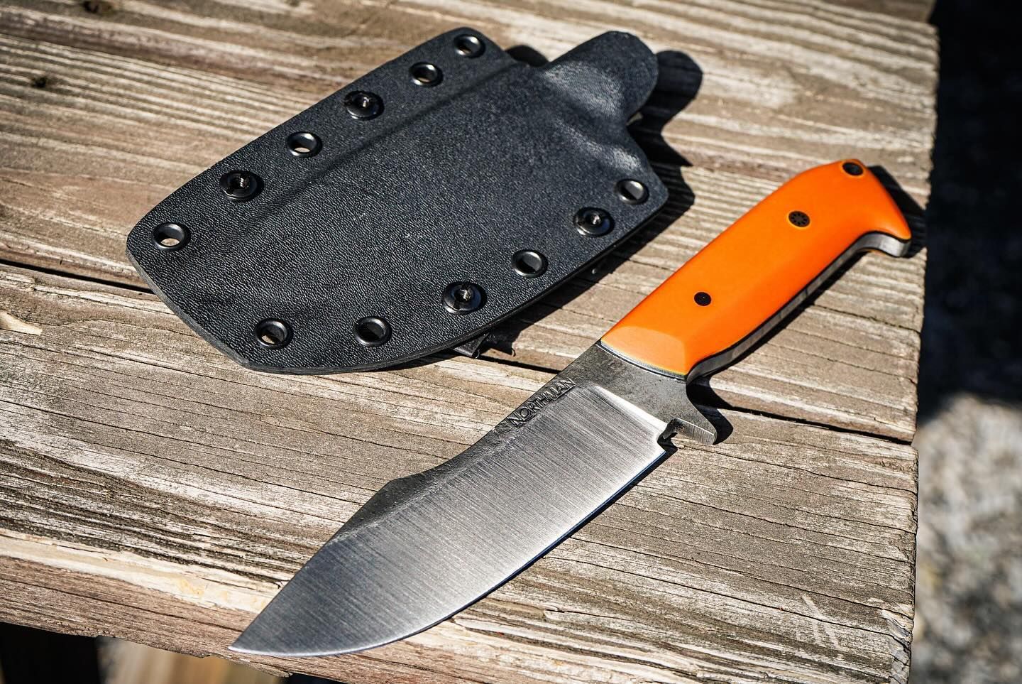 Hunting knife with orange handle and black sheath on a wooden surface.