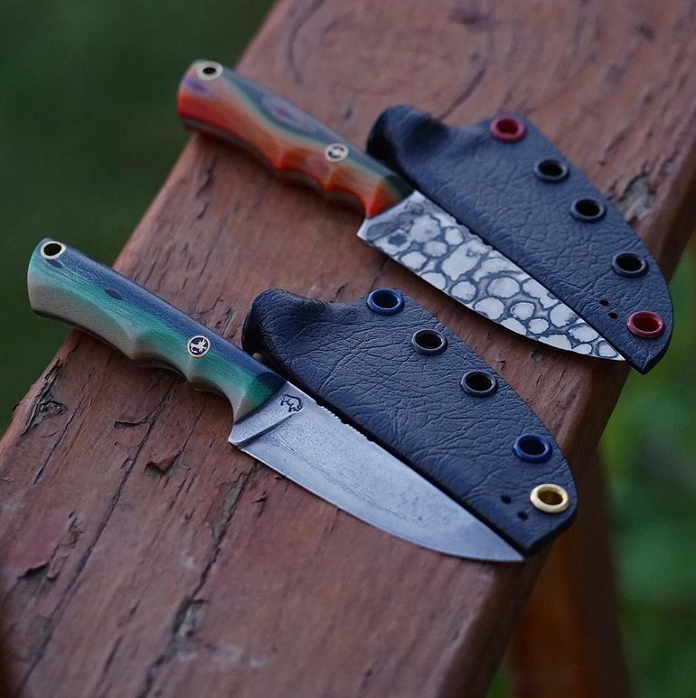 Two small knives with colorful handles and leather sheaths rest on a wooden surface.