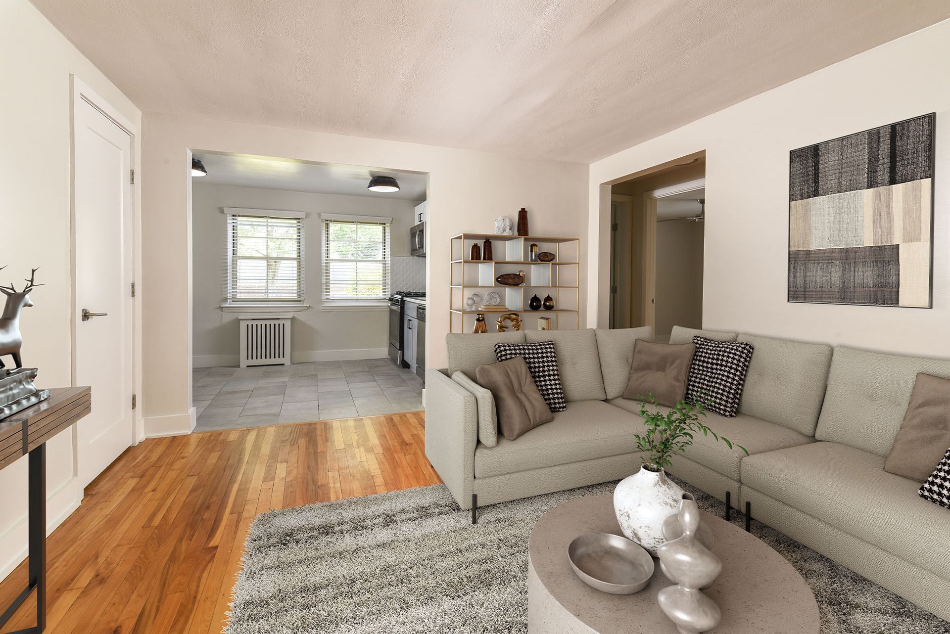 Living room with a light gray sectional sofa, neutral decor, and an open doorway to the kitchen.