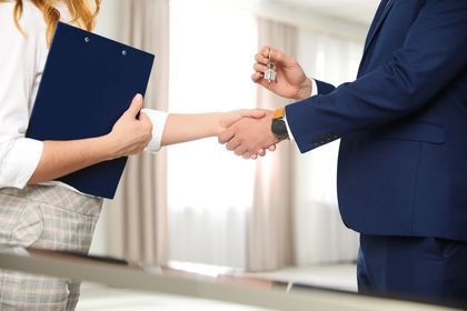 Due persone si stringono la mano in un ufficio, una delle quali tiene in mano una cartella blu.