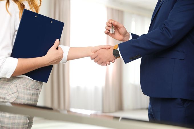 Due persone si stringono la mano in un ufficio, una delle quali tiene in mano una cartella blu.