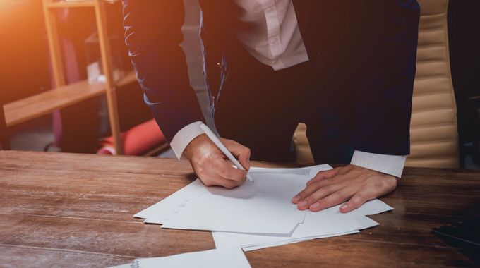 Un uomo in giacca e cravatta firma dei documenti su un tavolo di legno.