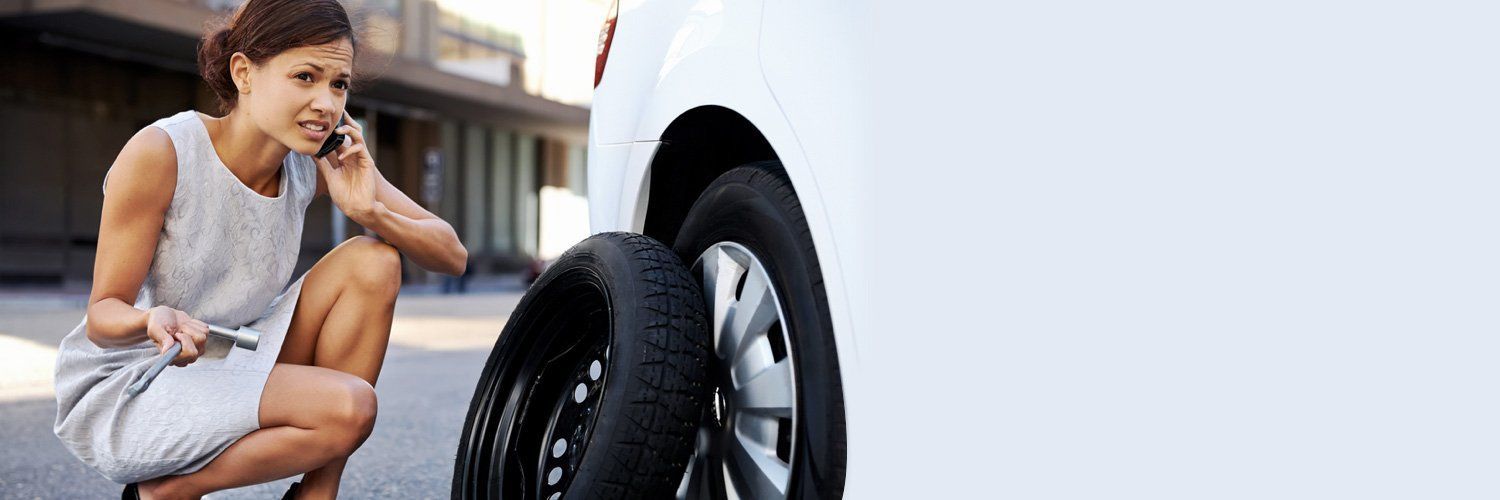 A Woman is Changing a Tyre on a Car While Talking on a Cell Phone — Hastings River Brake & Exhaust in Port Macquarie, NSW