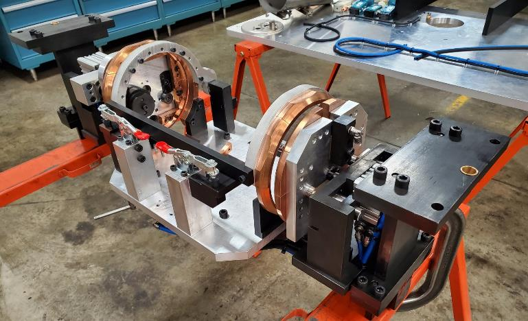 A complex mechanical assembly with copper coils, mounted on a stand in a workshop setting.