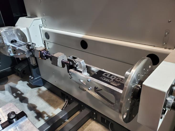 Machine holding a metal piece, likely for balancing. Gray and silver colors, industrial setting.