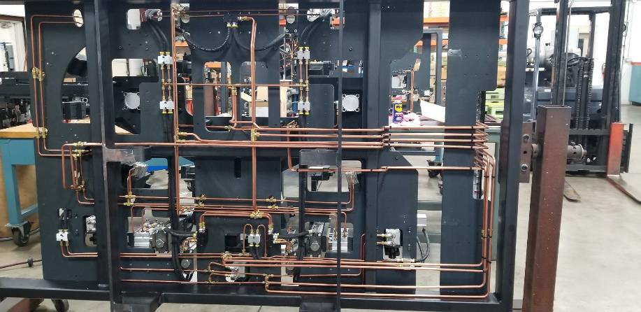 Black metal frame with copper tubing and various mechanical components. Industrial setting.