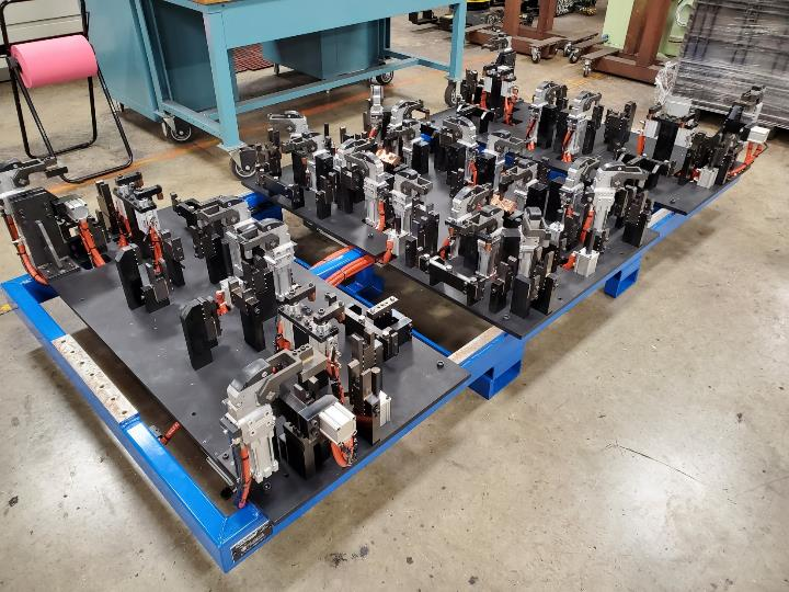 A blue metal base holds several black and silver clamps in a factory setting.