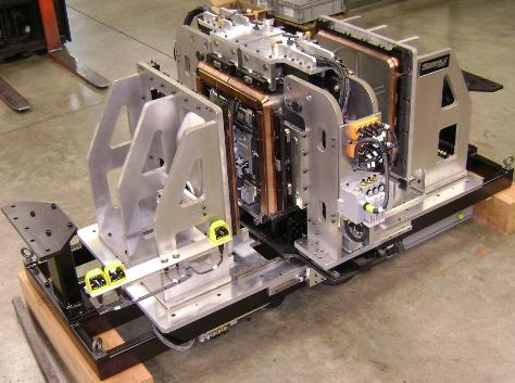Complex industrial machine with copper coils, mounted on a metal frame, resting on a wooden pallet.