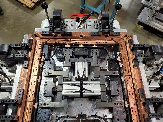 Metal welding fixture with clamps and levers, in a factory setting.