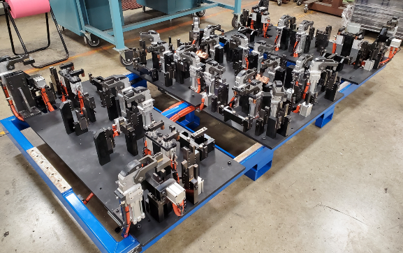 Metal manufacturing jigs on a blue cart in a factory setting.